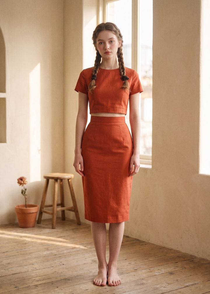 Woman wearing a rust-colored outfit standing in a sunlit room with wooden floor and beige walls.