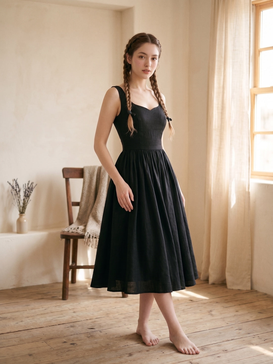 Woman in a black dress standing in a softly lit room with wooden floor and window.