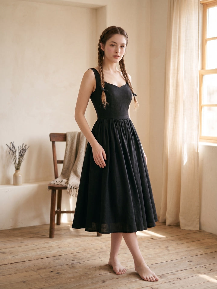 Woman in a black dress standing in a softly lit room with wooden floor and window.