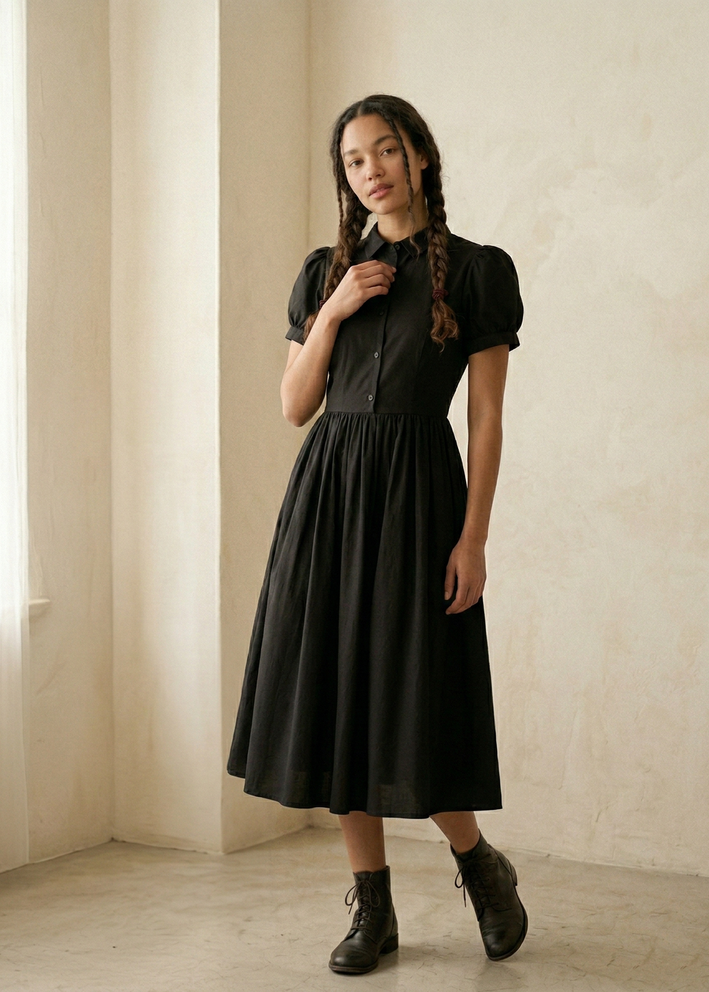 Woman wearing a black dress standing against a neutral wall.