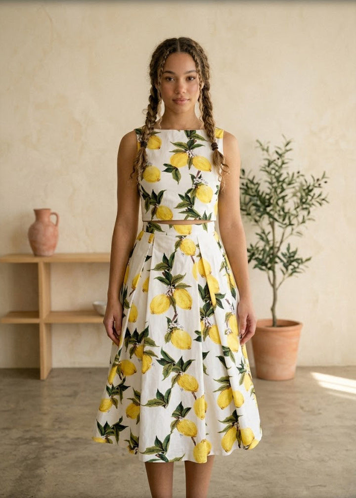 Woman wearing a dress with lemon pattern in a room with a plant and shelf.
