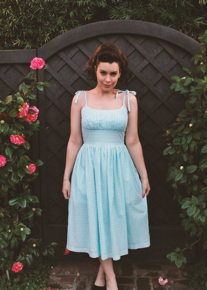 Woman in a light blue dress standing in front of a floral archway.