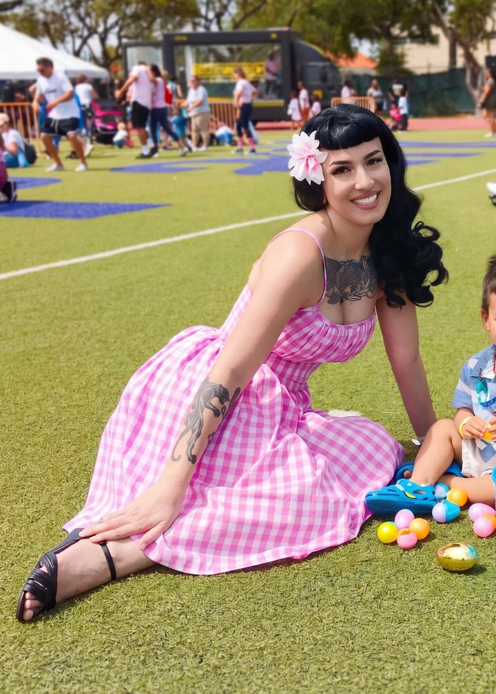 Woman in a pink dress sitting on grass with a child playing with toys