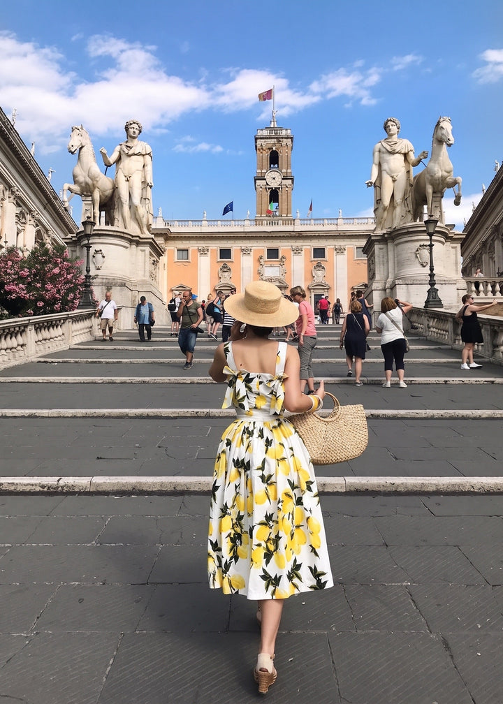 Woman in a yellow floral dress walking on steps with statues and architecture in the background