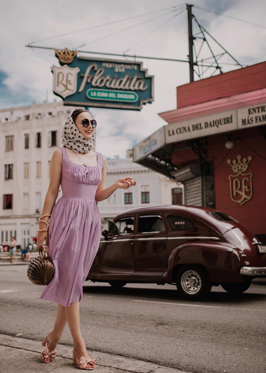 Woman in a purple dress standing in front of a vintage car and 'La Floridita' sign.