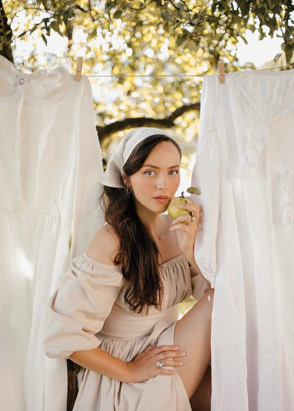 Woman in a beige dress holding an apple behind white curtains outdoors
