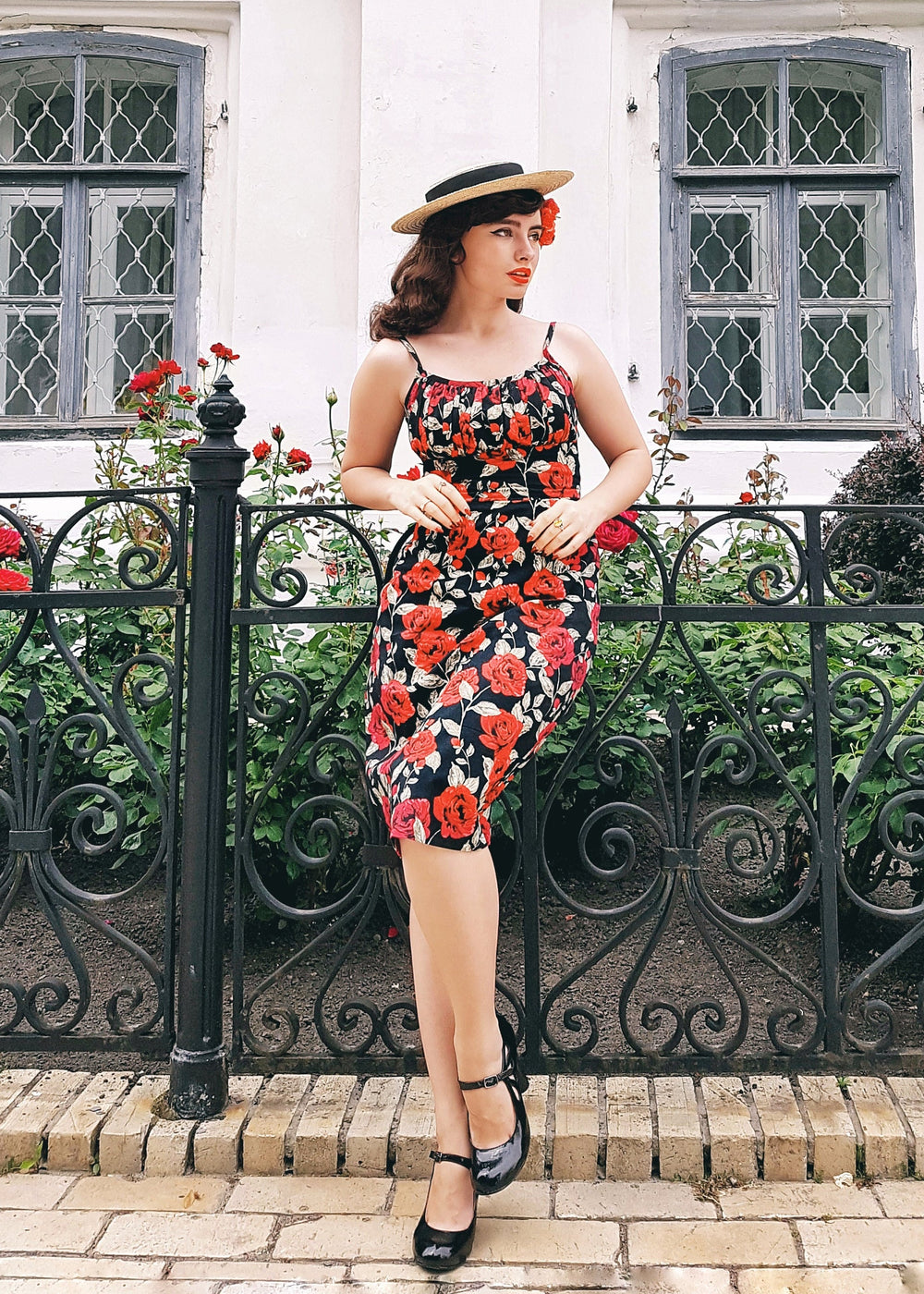 Woman in a floral dress standing in front of a white building with decorative windows and black iron fence.