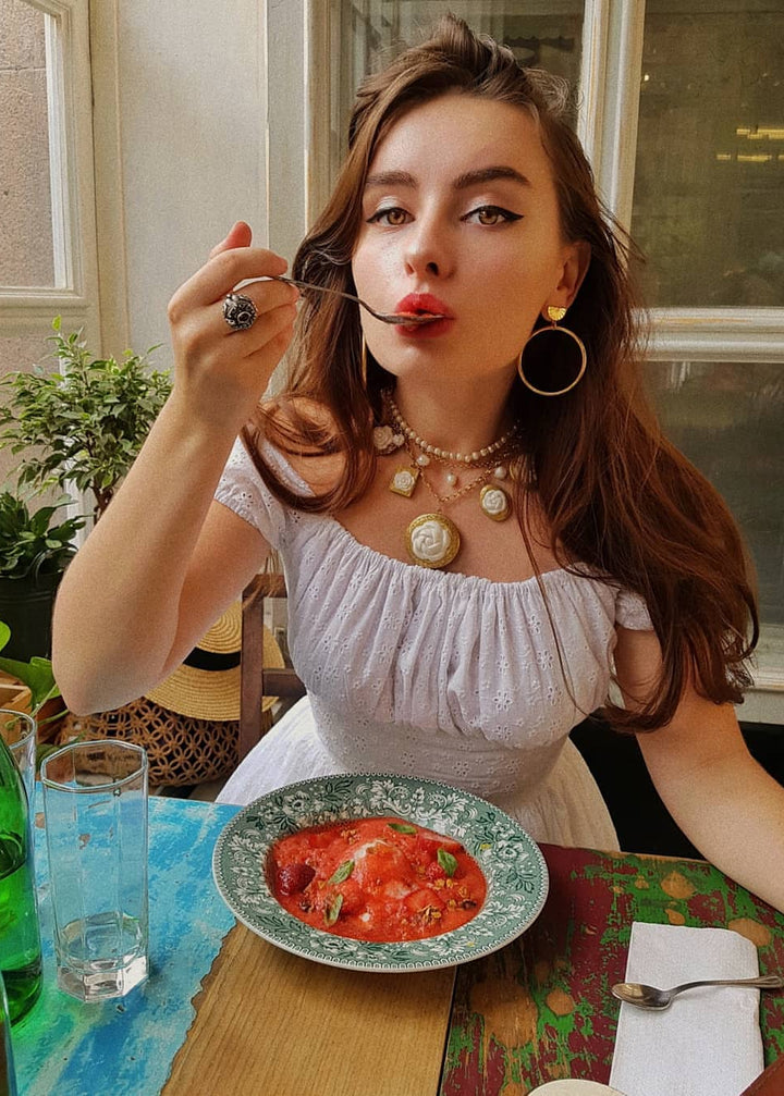 Woman eating from a plate of food at a table with a window in the background