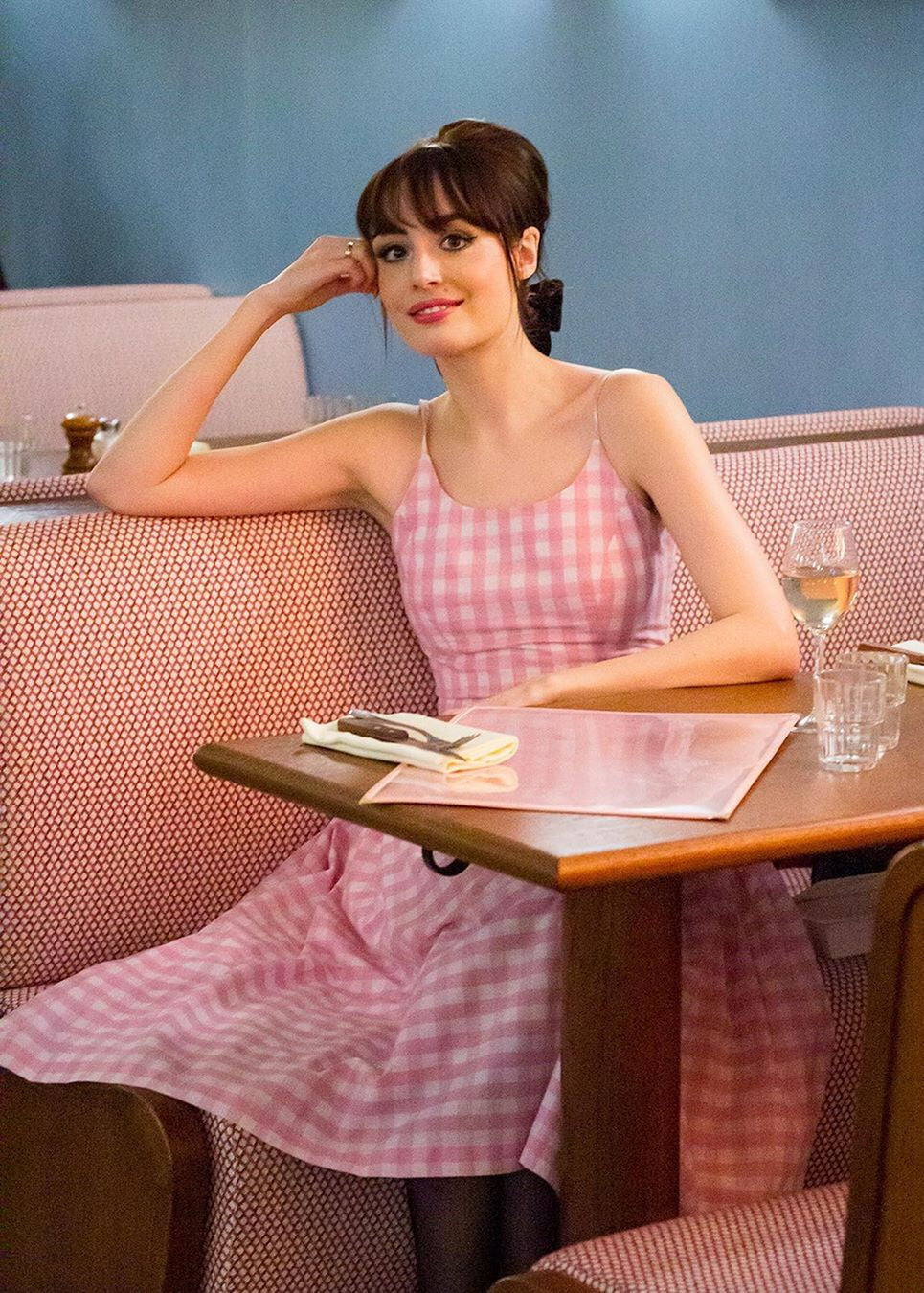 Woman in a pink checkered dress sitting at a table in a cafe.