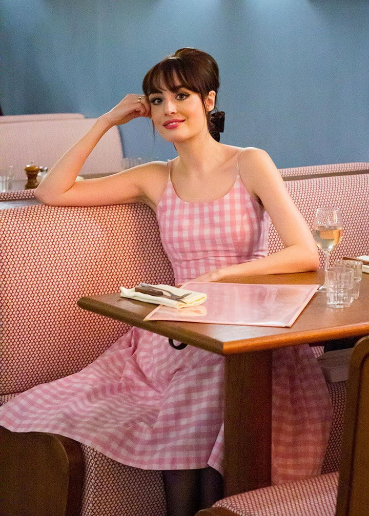 Woman in a pink checkered dress sitting at a table in a cafe.
