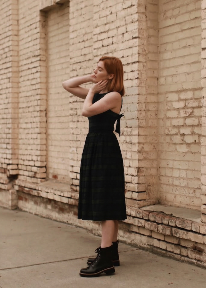 Woman in a black dress standing against a brick wall