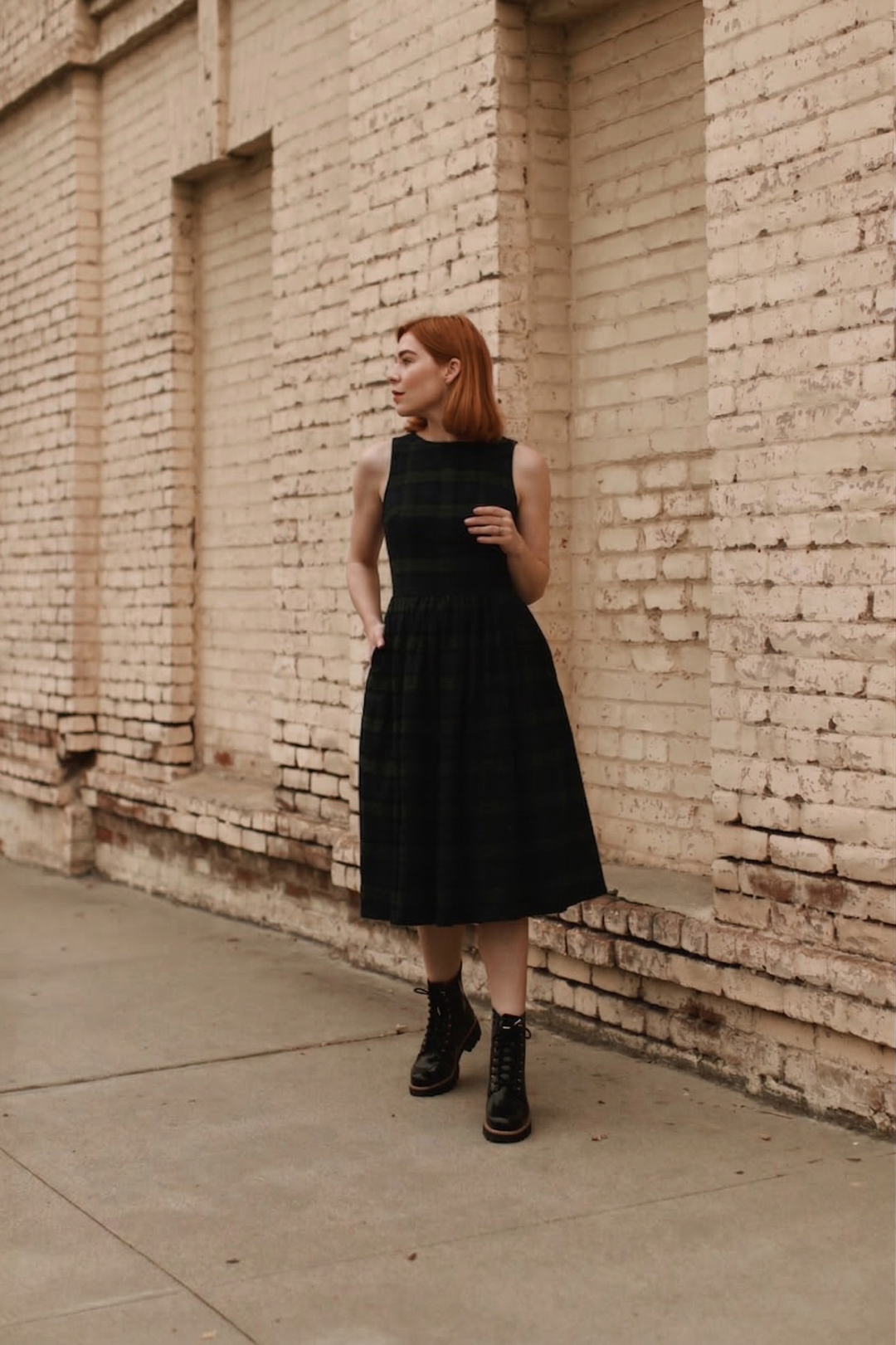 Woman in a plaid dress standing against a brick wall.