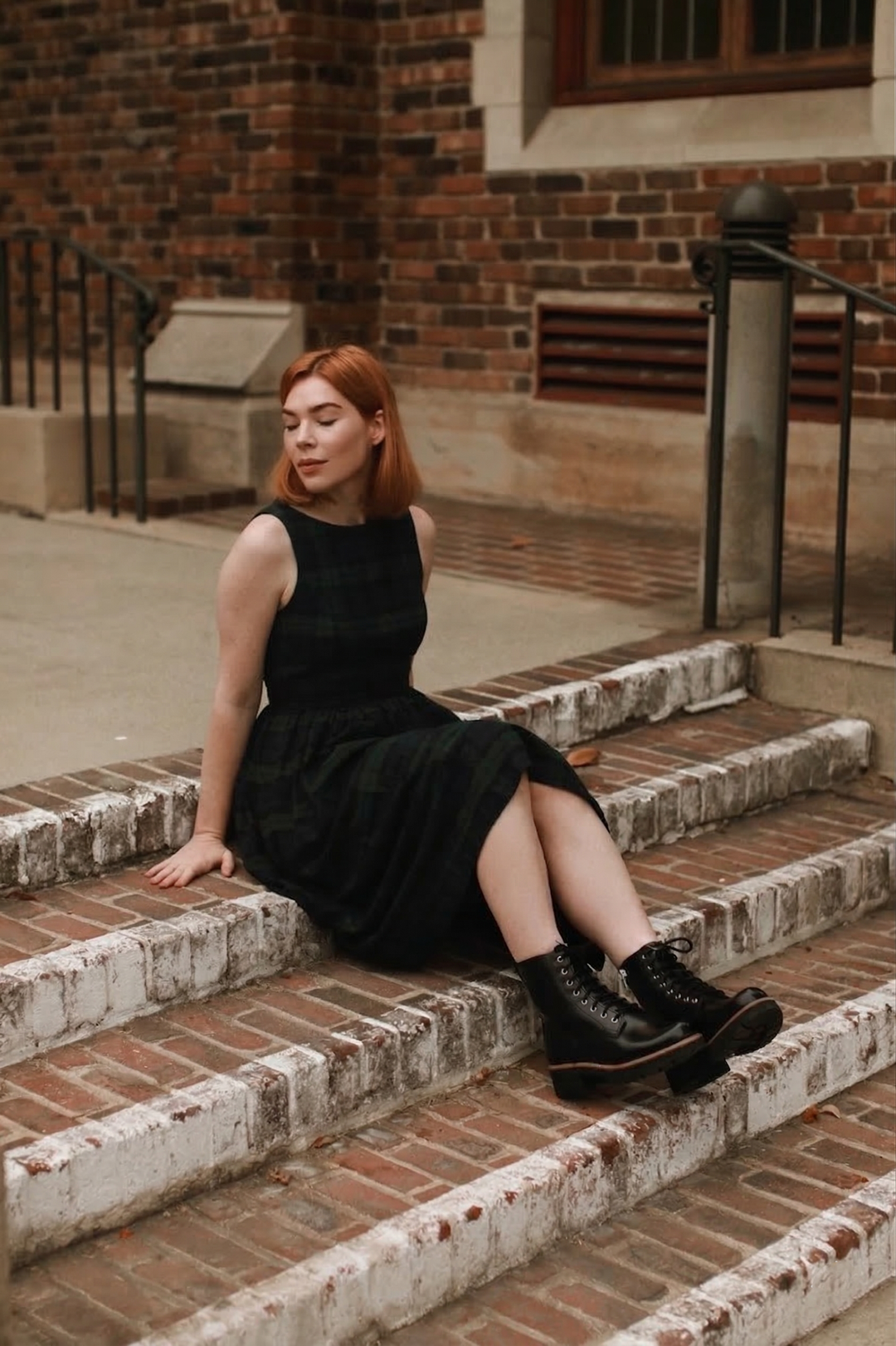 Woman in a plaid dress sitting on brick steps outdoors.