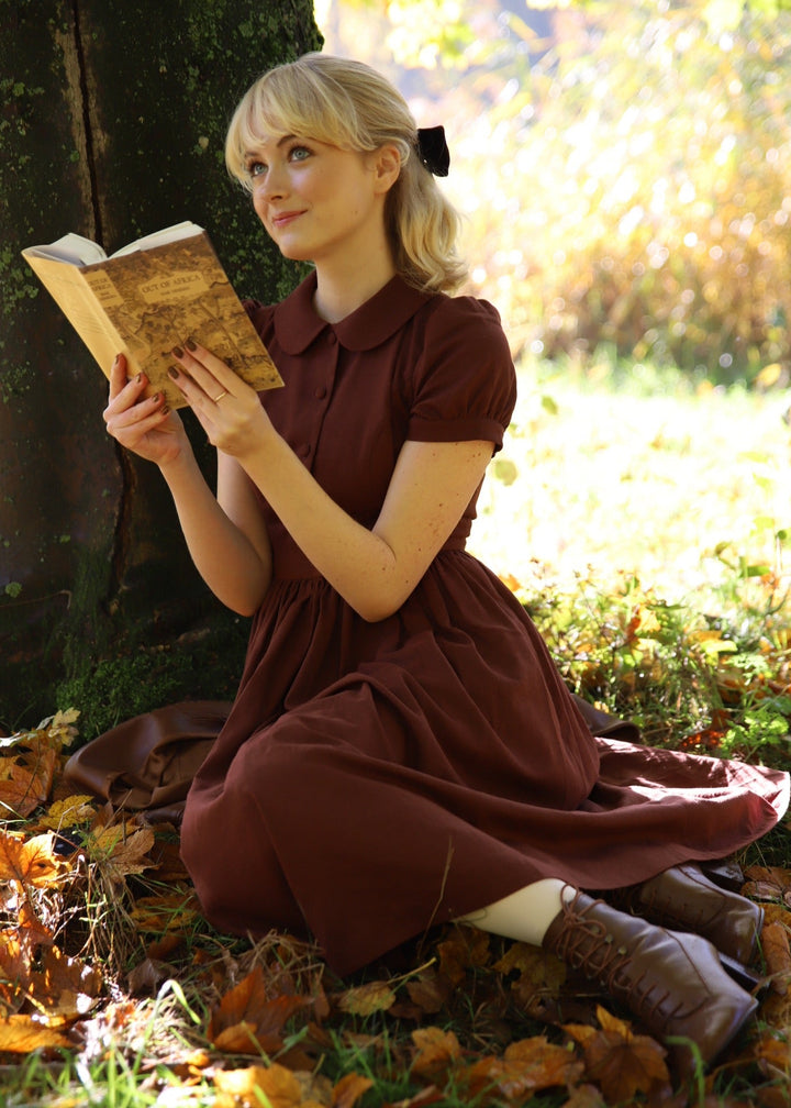 Woman in a brown dress reading a book in an autumn setting