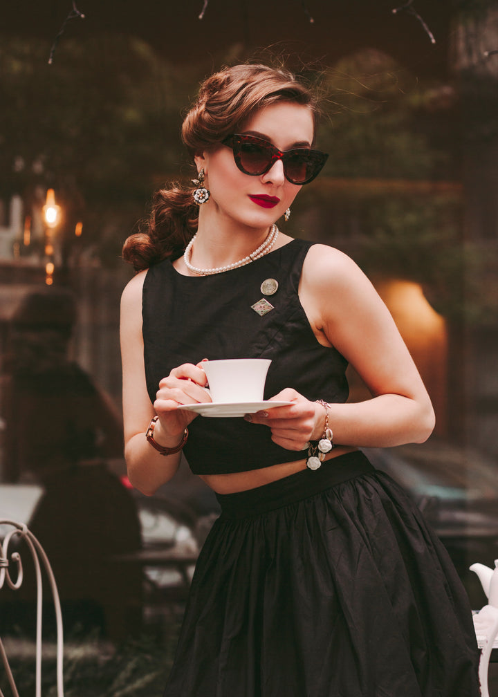 Woman in a black dress holding a cup outdoors with blurred background