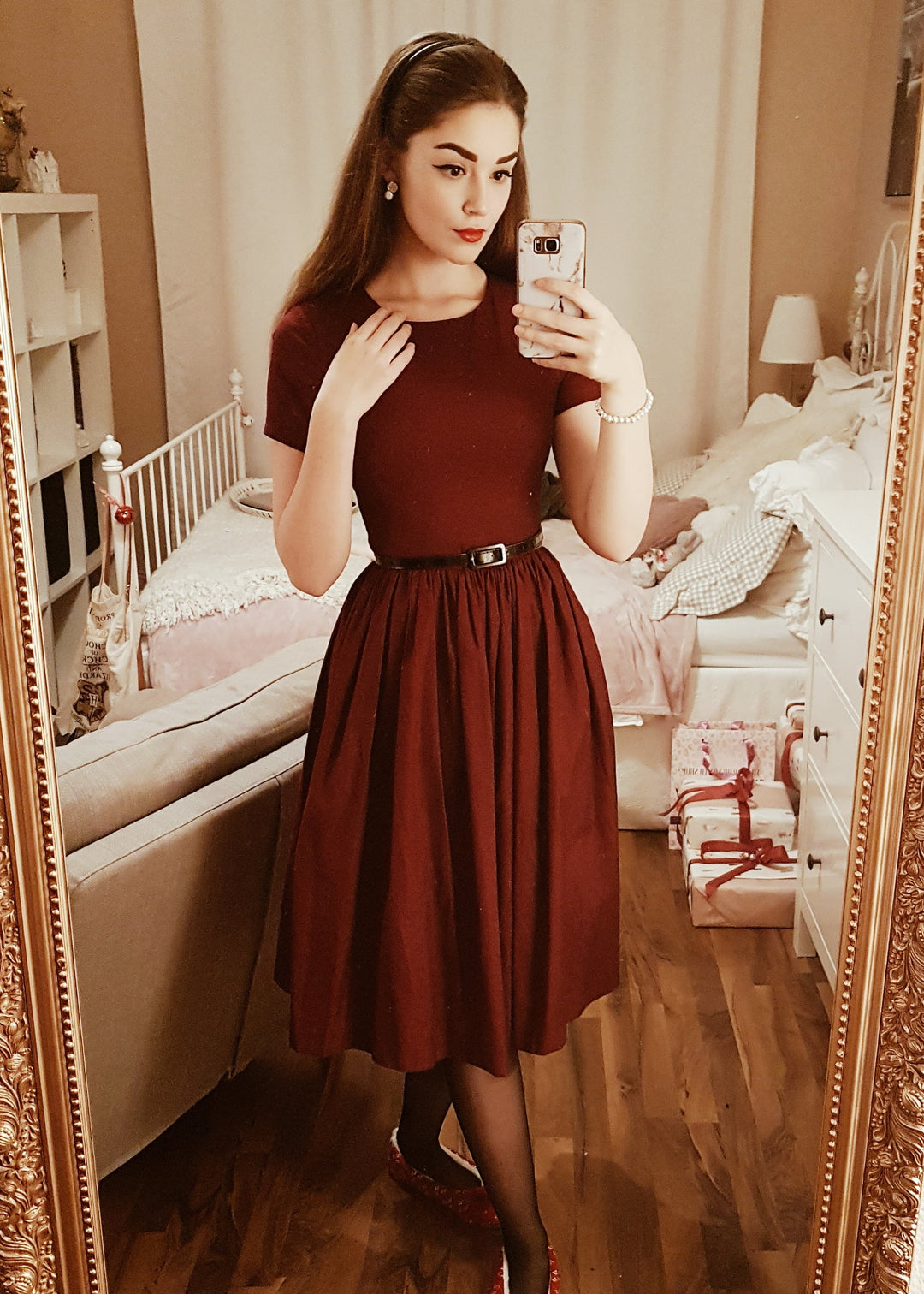 Woman taking a mirror selfie wearing a burgundy dress in a bedroom.