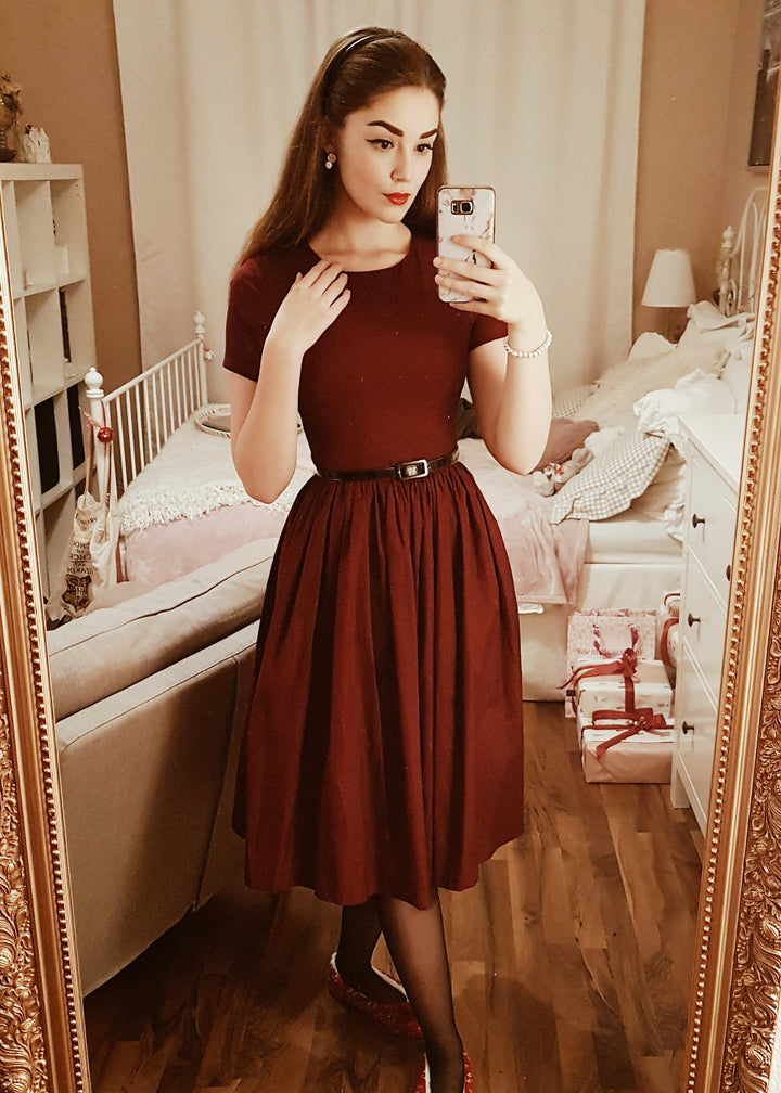 Woman taking a mirror selfie wearing a burgundy dress in a bedroom.