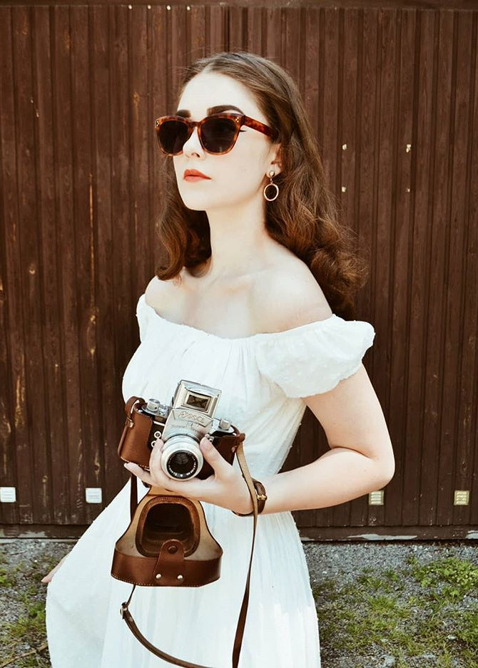 Woman in a white dress holding a vintage camera against a wooden background