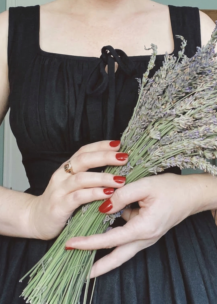 Woman with vintage hairstyle holding lavender flowers indoors.