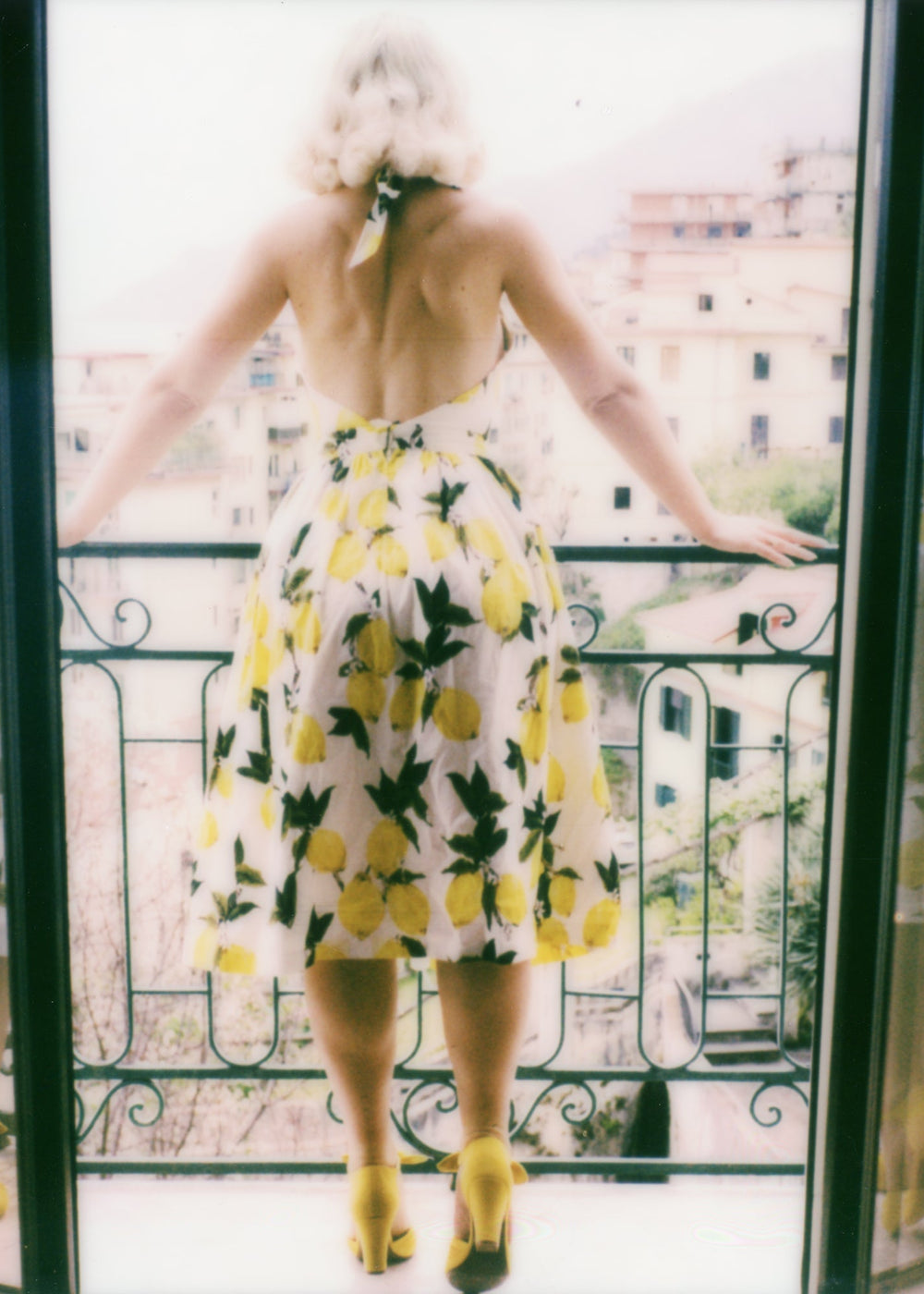 Person wearing a yellow and white dress with lemon pattern on a balcony.