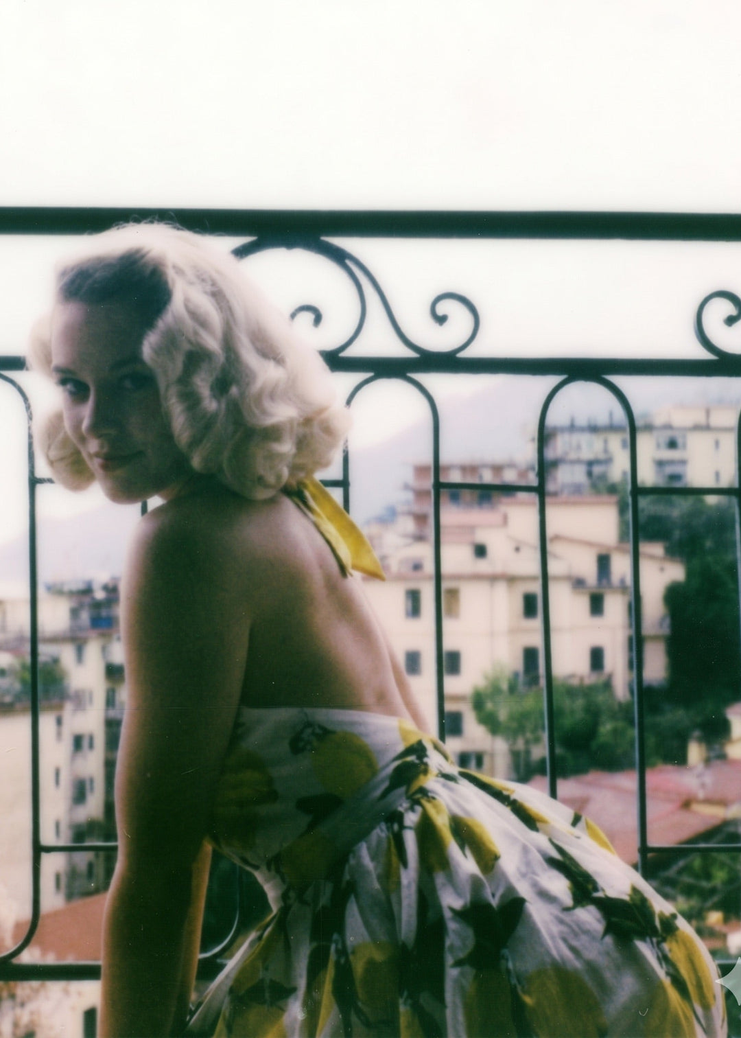 Woman in a floral dress standing on a balcony with an urban landscape in the background