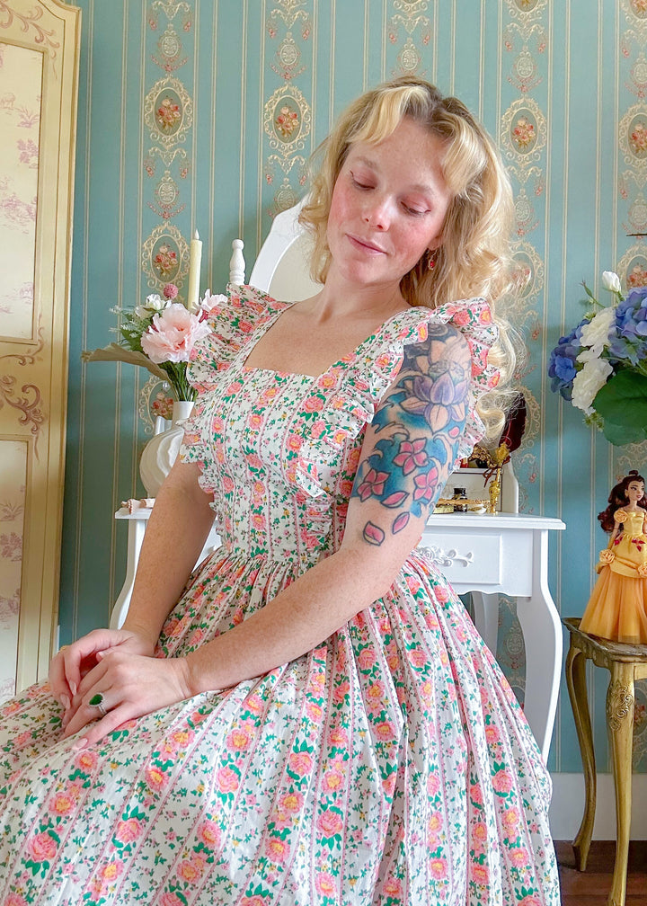 Woman in a floral dress sitting in a decorated room with wallpaper and decor.